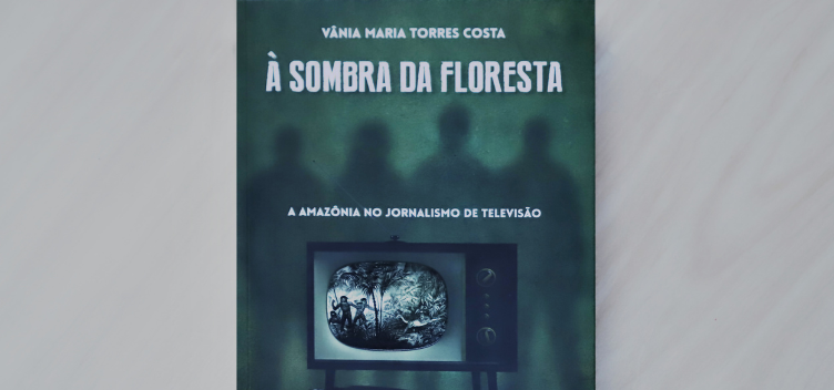 #ParaTodosLerem: Fotografia reproduz  a capa do livro “À sombra da floresta: A Amazônia no jornalismo de televisão. A capa tem fundo verde e a sombra de quatro pessoas. Ao centro, uma televisão, cuja tela  mostra  indígenas capturando uma onça em uma área de floresta. 