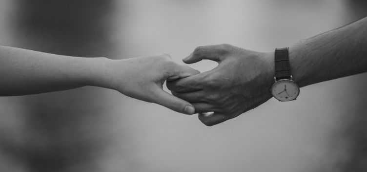 #ParaTodosVerem: Fotografia em preto e branco mostra duas mãos dadas. O enquadramento destaca ainda os dois antebraços, o da direita carrega um relógio na altura do pulso.