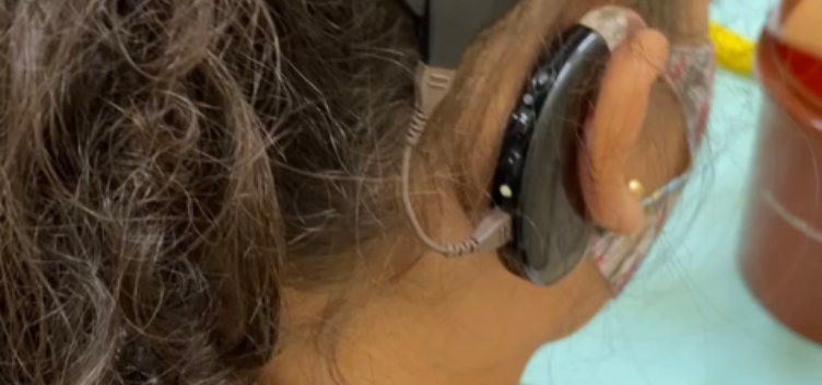 #ParaTodosVerem: Fotografia revela uma criança de costas. Ela está com o cabelo preso e usa um aparelho auditivo na orelha direita.